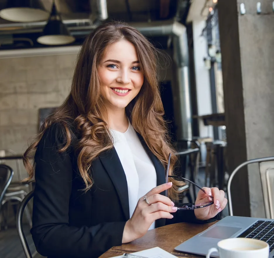 A businesswoman in a coffee shop with a laptop, she is looking at the camera and smiling