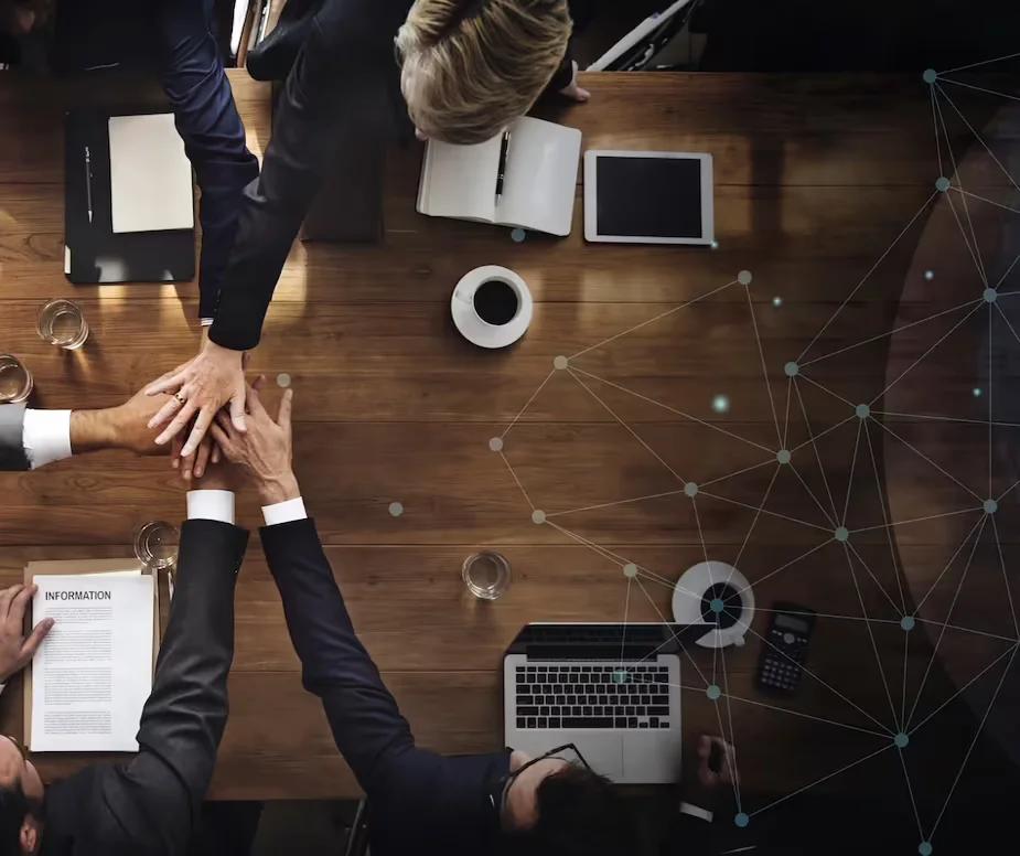 A top view of a business meeting on a wooden table with professionals in suits putting palms above each other and a translucent vector graphic of a nodal network over the image